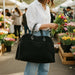 Person holding a black bag and flowers at an outdoor market.